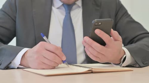 Close Up of Businessman Writing Information from Smartphone