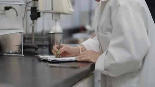 Wissenschaftlerin in weißem Kittel macht sich im Labor Forschungsnotizen zu Experimenten