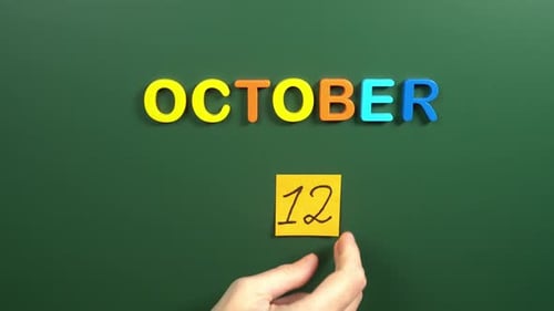 Hand sticking a sticker 12 October calendar day on school board. 12 date of October. Twelfth day