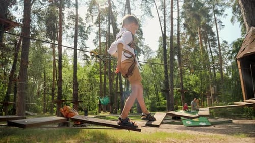 Little boy crossing wooden bridge in rope adventure park at forest