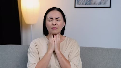 Frustrated Young Woman Touching His Neck While Sitting on the Couch at Home