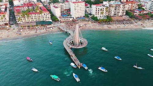 Drone flying over iconic pier in Puerto Vallarta at sunset. Beach full of tourists. Mexico
