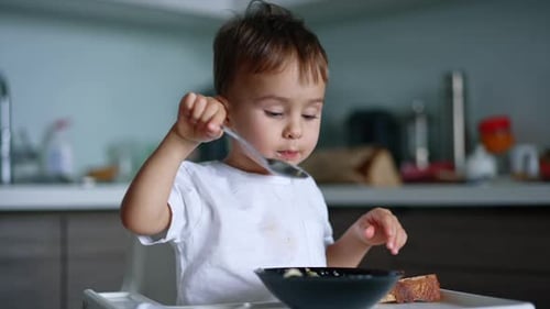 Menino caucasiano de cabelos escuros comendo sopa em uma tigela. Criancinha almoçando em casa. De perto.
