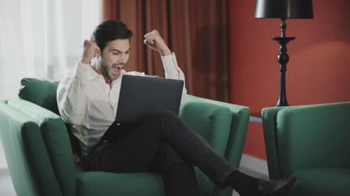 Excited man celebrates success while using laptop