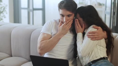 Shocked couple reacting to horrible news on laptop in modern home livingroom