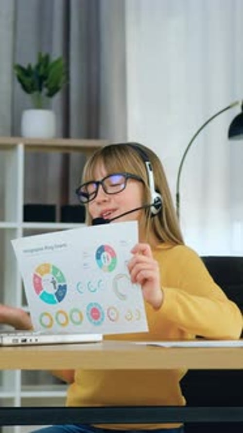Attractive Smiling in Good Mood Primary Schoolgirl in Headphones Sitting at Home at Her Workplace