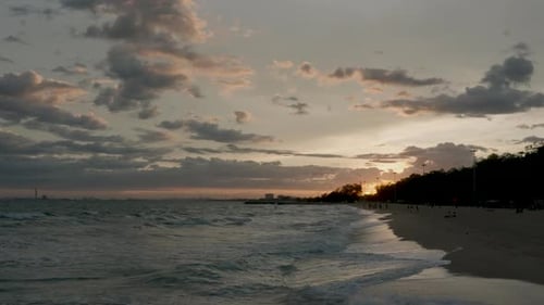 Waves roll gently across beach shoreline under golden twilight sky with soft clouds moving over hori