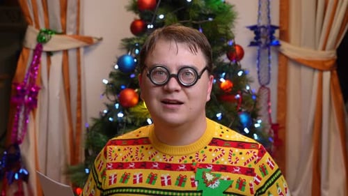 Homem lendo cartão em suéter festivo perto da árvore de Natal