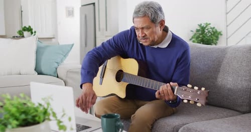 Man Plays Guitar at Home with Laptop