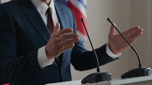 Man Speaks at Podium with Flags in the Background