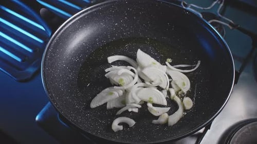 An overhead closeup of a hot oiled skillet where a man's hands transfer sliced onions then adds mult