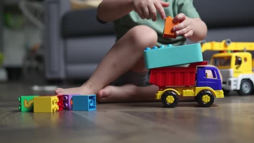 Child Plays with Toy Trucks and Blocks at Home