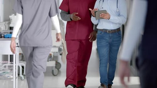 Diverse male doctors discussing work using tablet walking in hospital corridor, slow motion