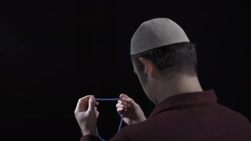 Man Counting Prayer Beads in Dark Room