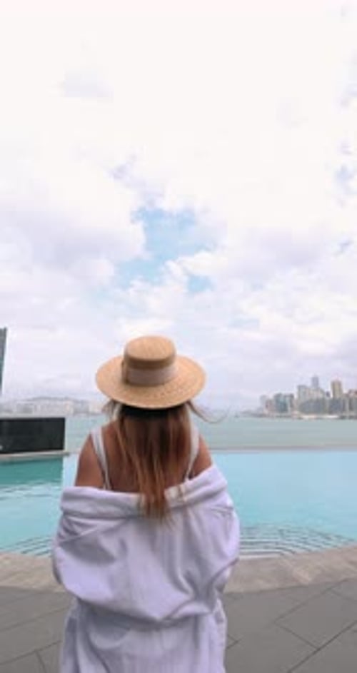Woman in White Bathrobe Walking to Infinity Pool with City Skyline