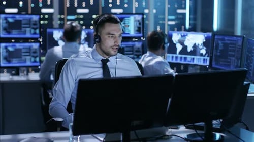 In System Control Center Technical Support Specialist Speaks into Headset while Sitting at His Desk