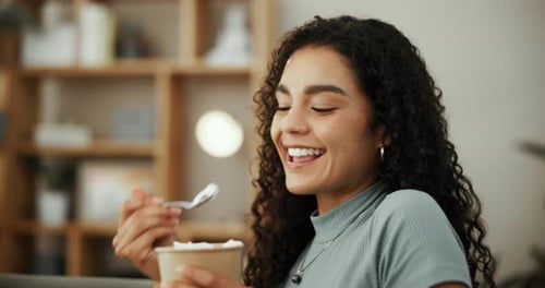 Mujer, comiendo helado y sonriendo con satisfacción en la sala de estar de la casa