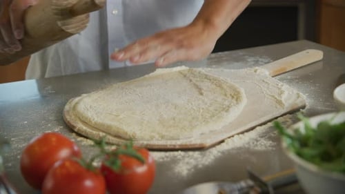 Man kneading and rolling fresh pizza dough in a bright kitchen