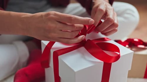 Adult hands tying bow on gift with red ribbon