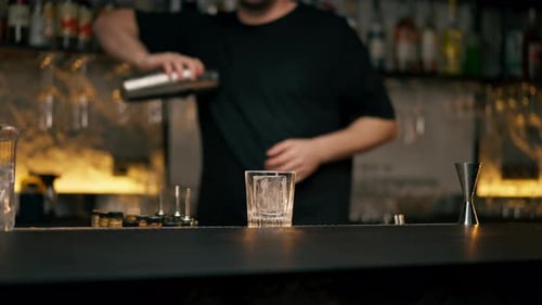 Young Male Bartender Apron Preparing Alcohol Drink Shaking It in Cocktail Shaker Standing in Front