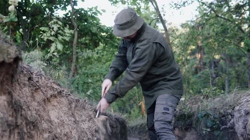 Soldier shovels a defensive dugout in woodland, sending dirt and dust into the air.