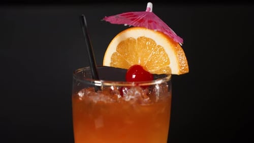 Tropical orange cocktail garnished with maraschino cherry orange slice and umbrella, close up 4K