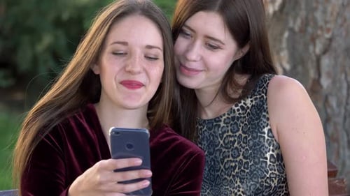 Two Young Women Using Smartphone Together Outdoors