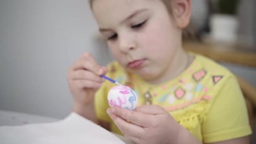 Girl Decorating Easter Egg with Watercolors Indoors