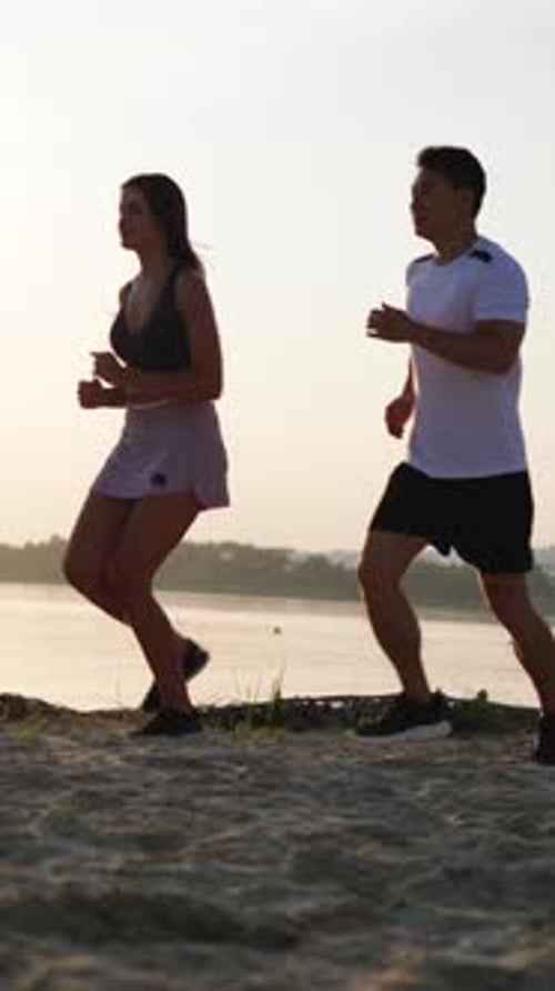A Couple is Jogging Together on a Beautiful Beach During the Vibrant Sunrise Enjoying the Moment