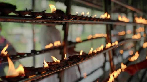 Rows of Burning Oil Lamps at Buddhist Temple Blur Worshiper in Background Devotees Perform Rituals