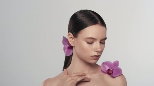 Young Brunette Female Model with Natural Makeup and Orchid Flower Looking at the Camera