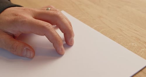 Nahaufnahme der linken Hand eines kaukasischen Mannes, der mit seinem Finger auf einem Stück Papier spielt.
Richtig