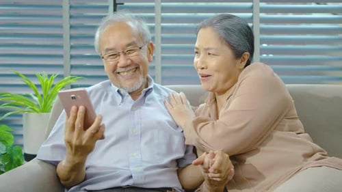Happy Mature Couple Using Phone on Couch