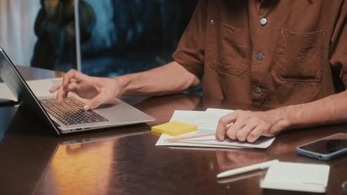 Person Typing on Laptop and Writing Notes at Desk