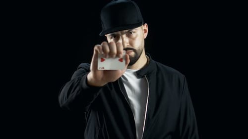Professional Street Magician in a Cap Performs Impressive Sleigth of Hand Card Trick. Background is