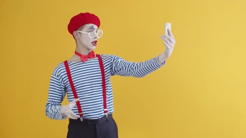 Studio Portrait of an Emotional Male Mime Artist Talking on a Video Call on His White Smartphone