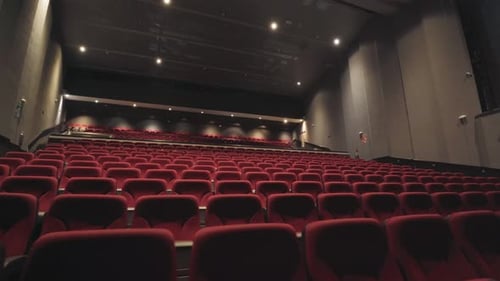 Slow dolly shot along rows of red cinema seats with bright lights