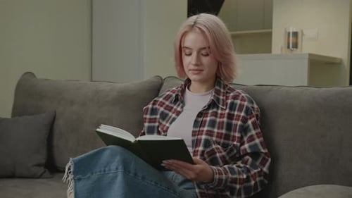Young Woman Reading a Book on Couch Indoors