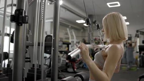 Sporty female woman in grey suit pulled on sports simulator in gym. Back muscles are very tense.