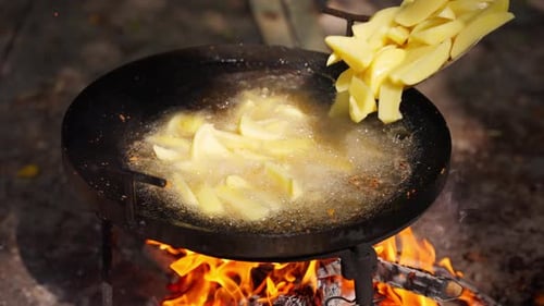 Potatoes being fried in a pan over open fire
