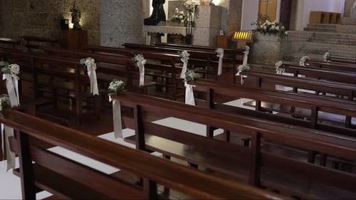 Wooden church pews decorated with delicate white flowers and ribbons for a wedding ceremony