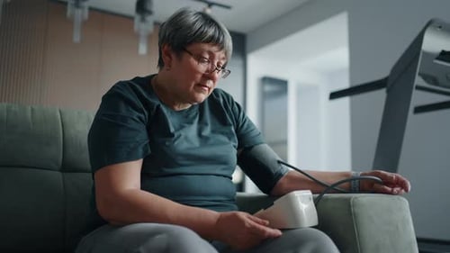 Übergewichtige Seniorin misst zu Hause den Blutdruck mit einem modernen Elektronisch Blutdruckmessgerät