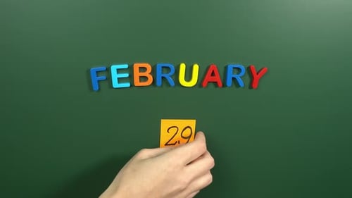 Hand sticking a sticker 29 February calendar day on school board. 29 date of February. Twenty ninth