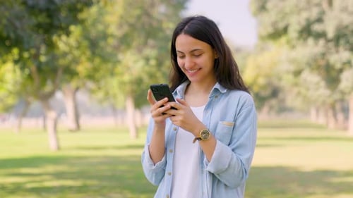 Smiling Woman Using Smartphone in Green Urban Park