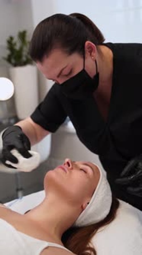 Un esteticista con uniforme negro realiza una limpieza facial con espuma en la rutina de cuidado de la piel del cliente en el salón