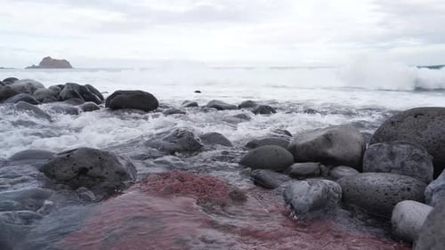 View of a pebble beach, cristal clear water flowing down the river mouth into the sea, waves crushin