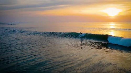 Surfer catching a wave under a stuning sunset