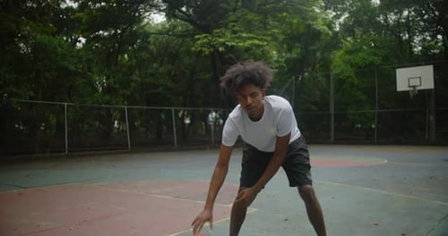 African descent man practicing dribbling on outdoor basketball court, moving with control and