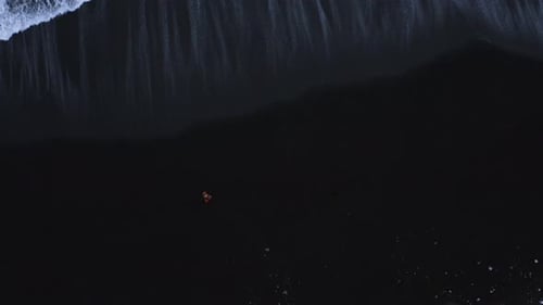 Man Walking Along Black Sand Beach In Iceland With Atlantic Waves. - aerial top down