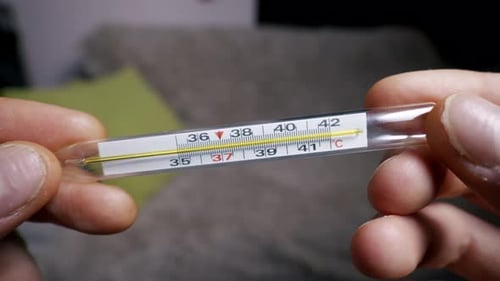 Männliche Hände, die ein Glasthermometer halten und hohe Fiebertemperatur anzeigen